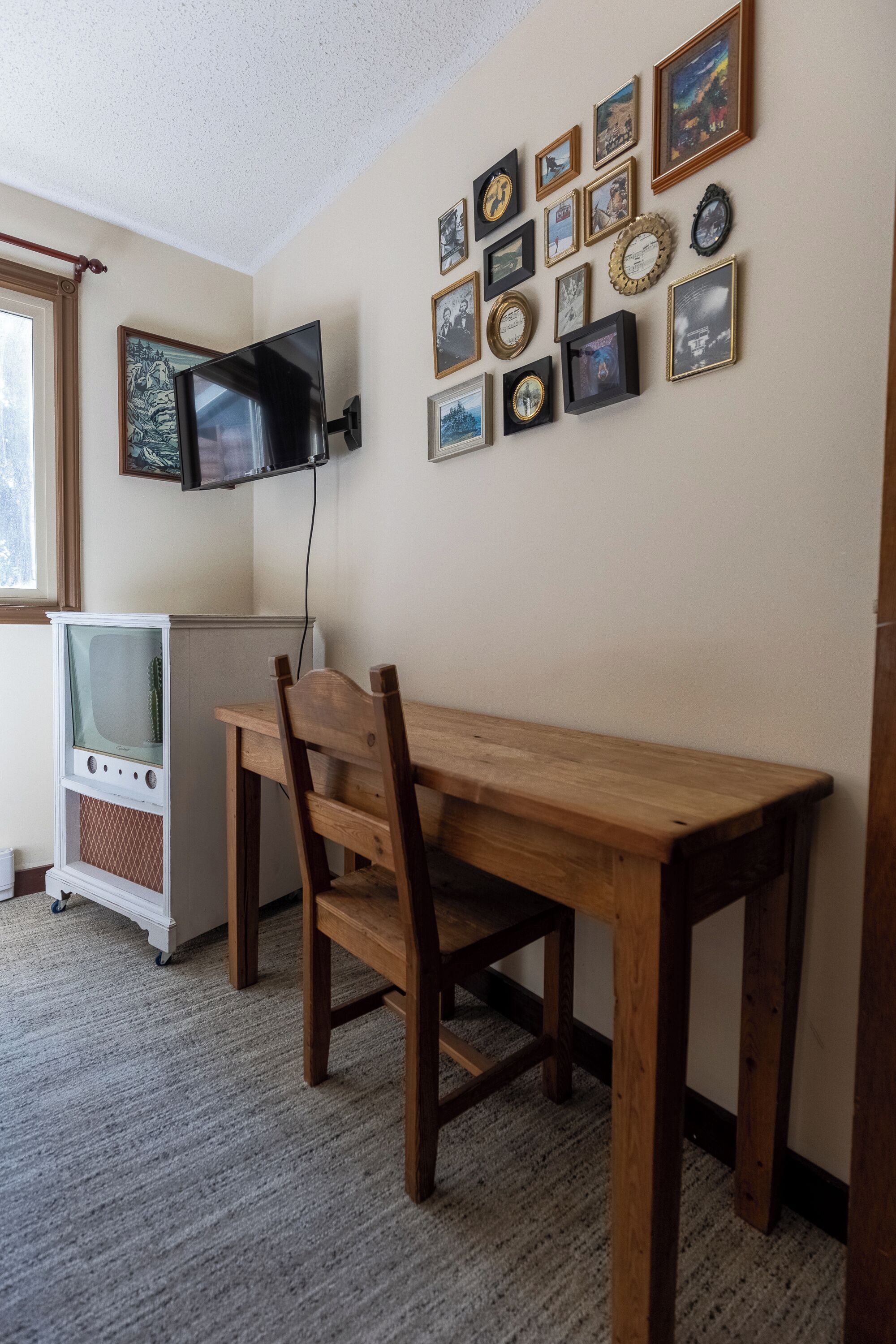 Una habitación con una mesa y silla de madera, un televisor antiguo y una pared decorada con cuadros.