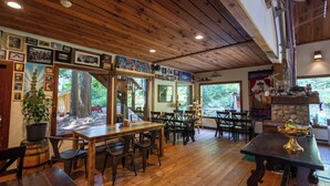 A rustic interior with wooden floors, tables, and chairs, framed pictures on the walls, and a stone fireplace. - Rams Head Inn (Rossland)