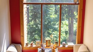 A cozy room with two armchairs, a wooden table, and a large window offering a view of a forest. - Rams Head Inn (Rossland)