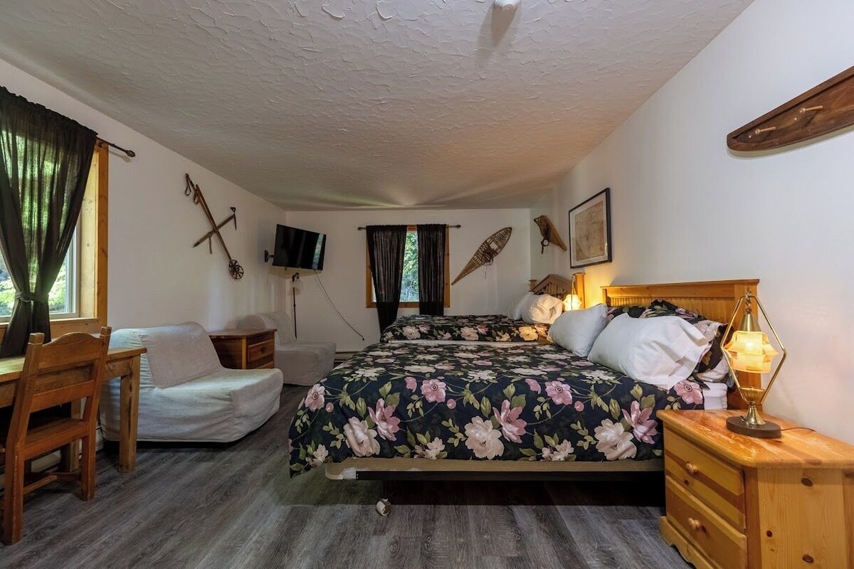 A bedroom with a bed, bedside table, lamp, wooden furniture, and a TV mounted on the wall.