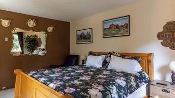 A bedroom with a wooden bed, floral bedding, a mirror, and two framed pictures on the wall.