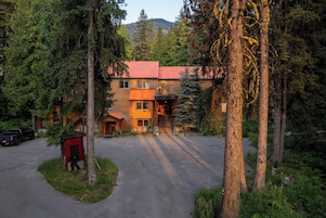 Una cabaña con techo rojo, rodeada de altos árboles y una montaña al fondo.