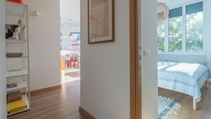 A bedroom with a bed, a window with a view of trees, a wooden floor, and a hallway with shelves and a door. - Green Home Seaside Parking  Wifi Ac Genova (Genoa)