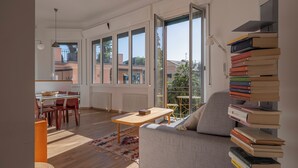 A modern living room with a sofa, a dining table, and a bookshelf filled with books. - Green Home Seaside Parking  Wifi Ac Genova (Genoa)