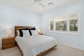 A bedroom with a bed, two bedside tables, a ceiling fan, and a window with blinds.