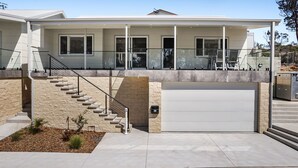 Une maison moderne à deux étages, dotée d’un porche abrité, d’un garage et d’un escalier en pierre.