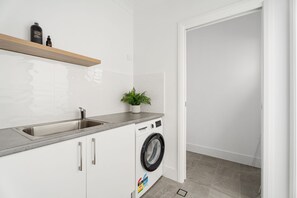 A modern laundry room with a stainless steel sink, a washing machine, and a shelf with toiletries.