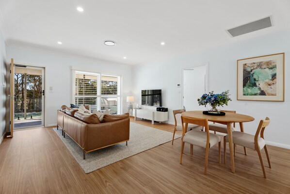 A modern living room with a brown leather sofa, a dining table with chairs, and a painting on the wall.