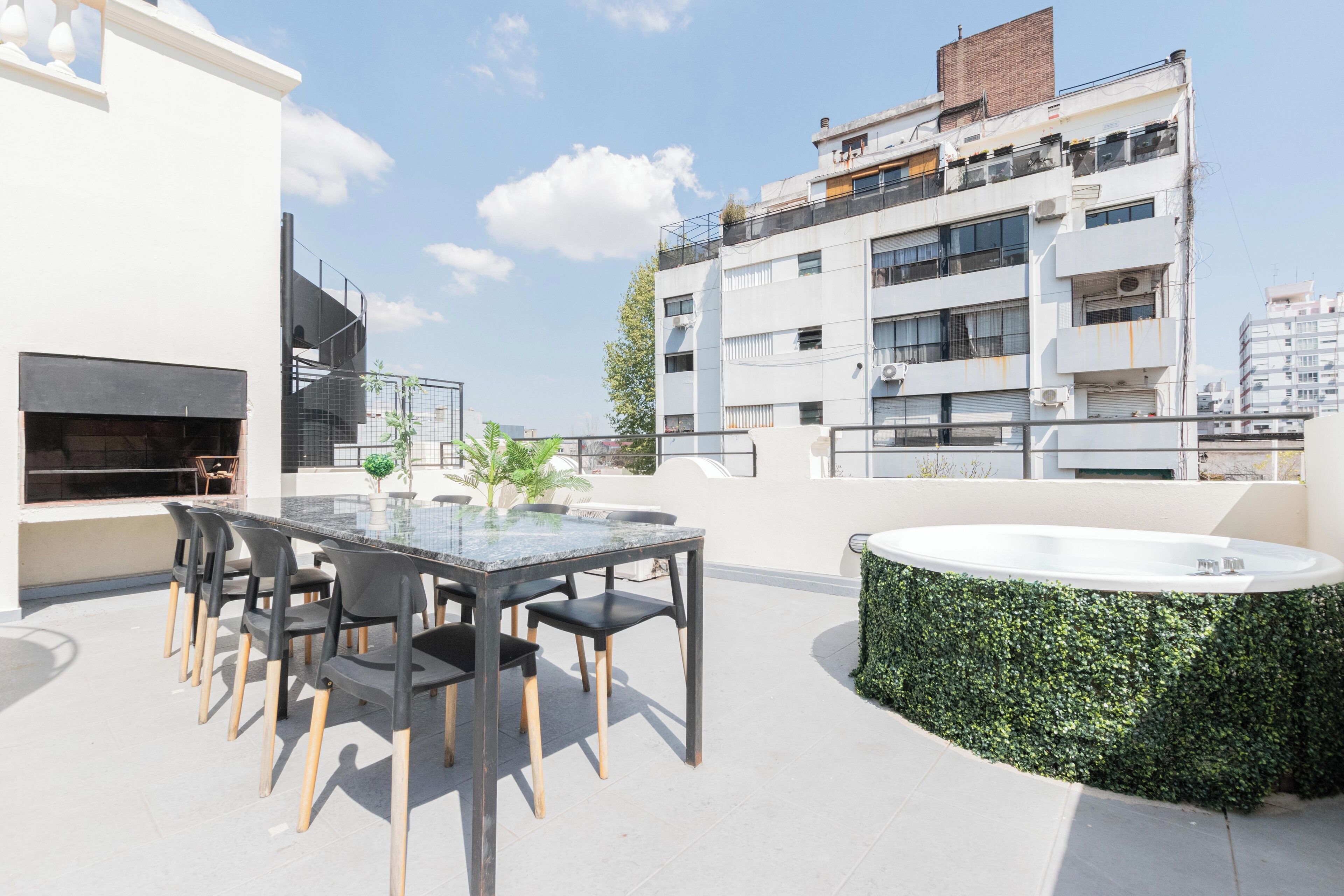 Una terraza en la azotea con mesa y sillas de vidrio, un jacuzzi y vistas de un edificio moderno.
