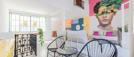 A spacious room with a white sofa, black chairs, and a large window with yellow diamond patterns.