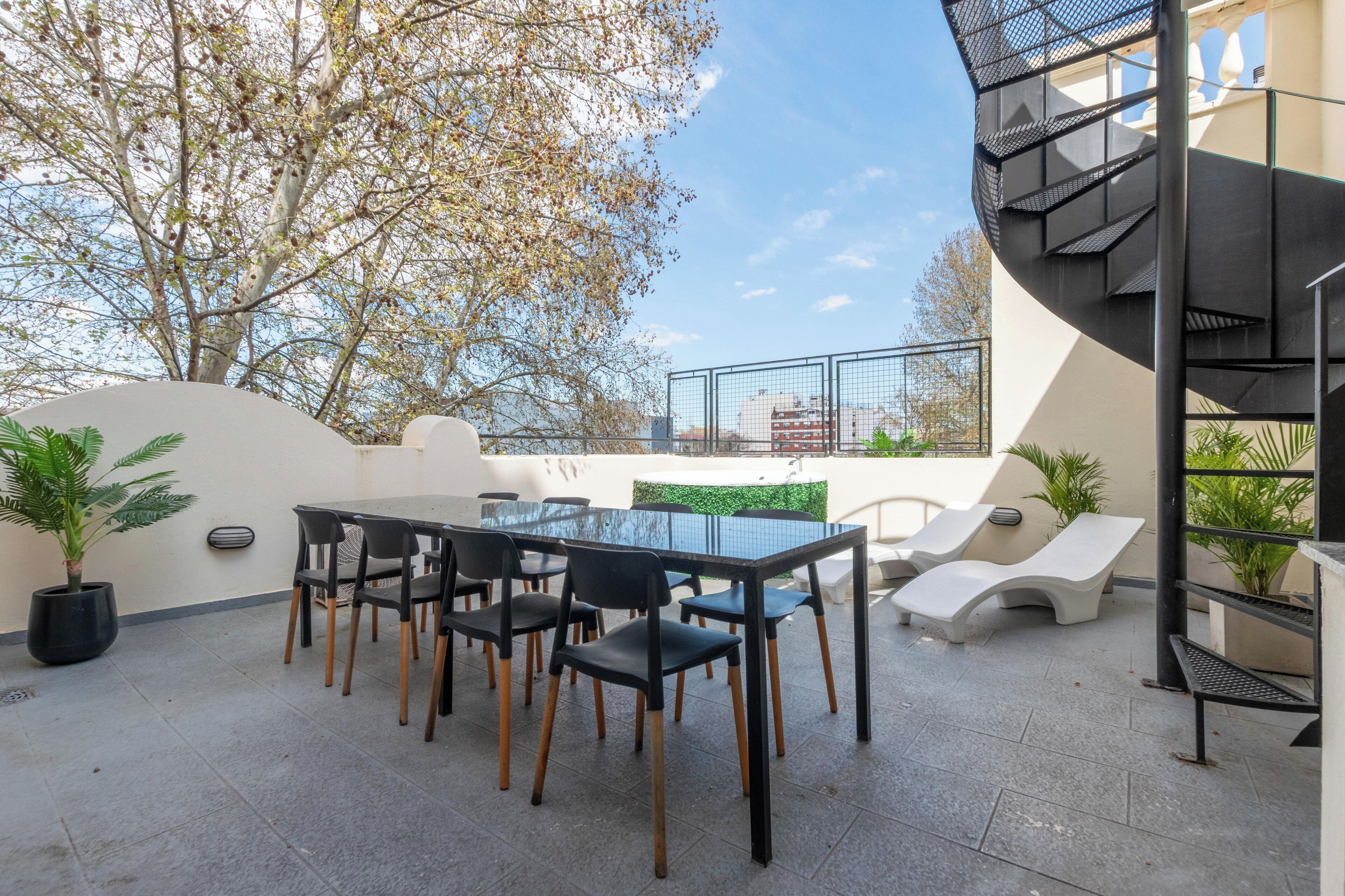 Eine Dachterrasse mit Glastisch und Stühlen, umgeben von Topfpflanzen und einer modernen Treppe.