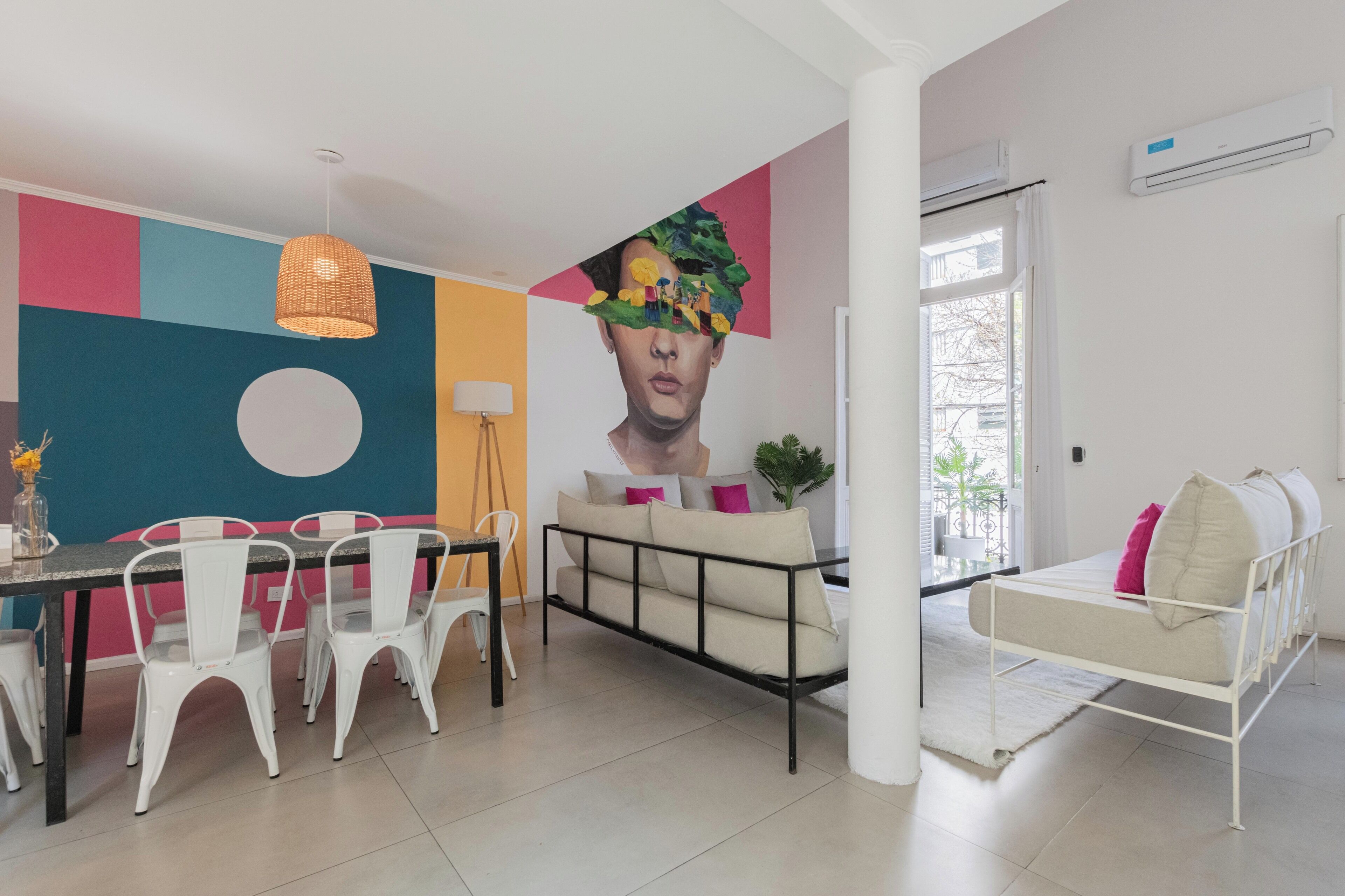 A modern living room with a dining area, featuring a sofa, chairs, a table, and a large abstract painting on the wall.