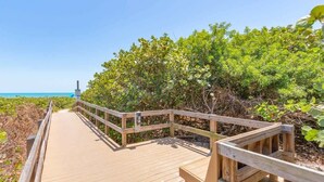 A wooden boardwalk leading to a beach with dense vegetation on either side. - Ocean's Edge Retreat- Direct Ocean 2 Bed/2Bath (Cape Canaveral)