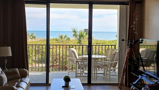 A room with a balcony overlooking the beach, furnished with a sofa, a table, and chairs. - Ocean's Edge Retreat- Direct Ocean 2 Bed/2Bath (Cape Canaveral)