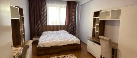 A bedroom with a bed, a desk, a chair, and built-in shelving.