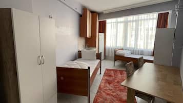 Habitación de hotel compacta con cama, kitchenette pequeña, mesa de comedor y un amplio armario.