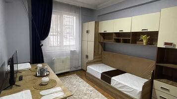 A hotel room with a bed, a desk with a chair, a TV, a window with curtains, and built-in cabinets.