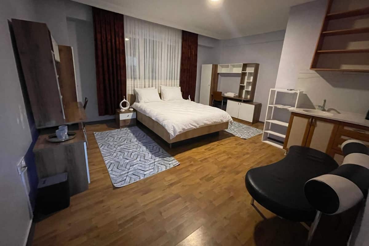 Un dormitorio moderno con cama, mesitas de noche, un escritorio, una silla y un espejo.