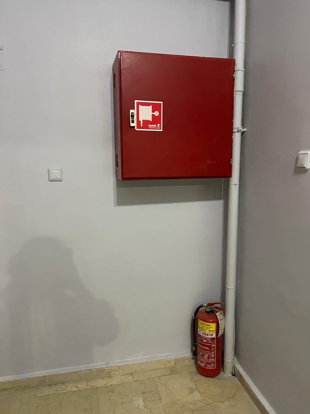 A red fire safety cabinet mounted on a wall with a fire extinguisher placed on the floor beside it.