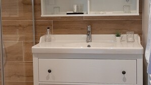Une salle de bain avec un meuble-lavabo blanc, un grand miroir et une cabine de douche en verre.