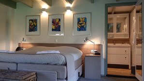 Une chambre à coucher avec un lit, des tables de chevet, une lampe et une plante suspendue. Trois œuvres d’art encadrées ornent le mur.