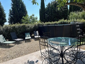 Une terrasse avec une table et des chaises en verre, entourée d’une zone recouverte de gravier et d’un feuillage dense.