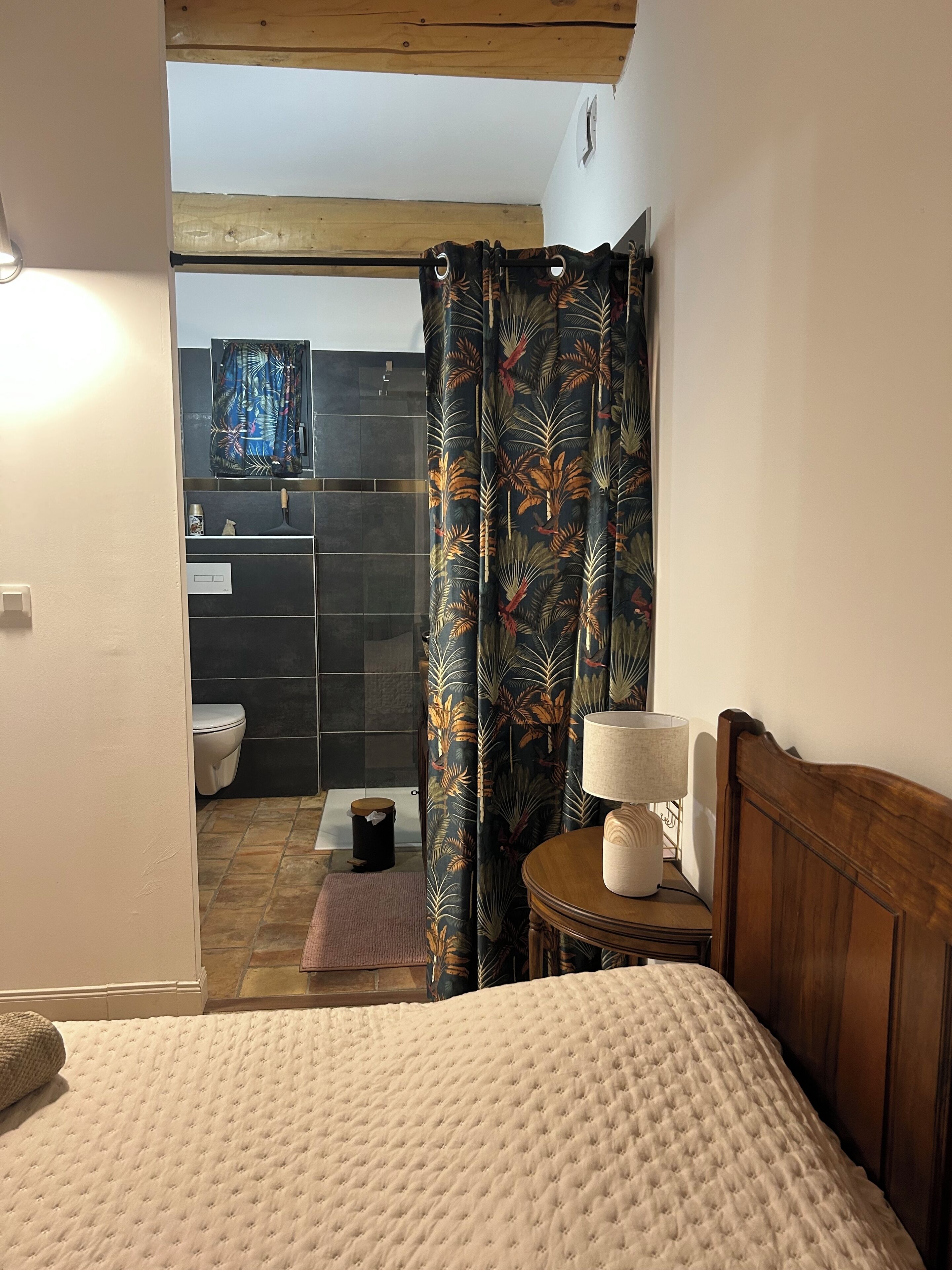 Una camera da letto con un letto, una testata imbottita in legno, un comodino con una lampada e un bagno visibile attraverso una porta aperta.