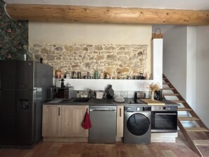 A kitchen with a stone wall, wooden beams, a dishwasher, a washing machine, and a microwave.