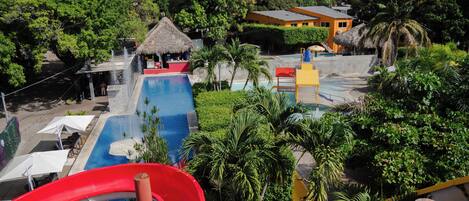 A water park with multiple pools, a red slide, and thatched-roof structures.