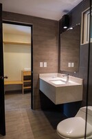 Un baño moderno con un lavamanos integrado, un inodoro y un espejo. Hay un estante de madera y un perchero.