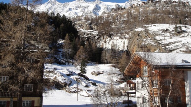 Un chalet de montagne à l’extérieur en bois, entouré d’un paysage enneigé et d’arbres.