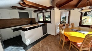 Une cuisine moderne avec un îlot central en bois, un coin repas doté d’une table jaune et de chaises en bois.