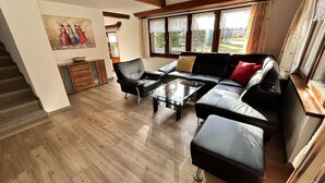 Un salon moderne avec un canapé, des fauteuils, une table basse en verre et un tableau accroché au mur.