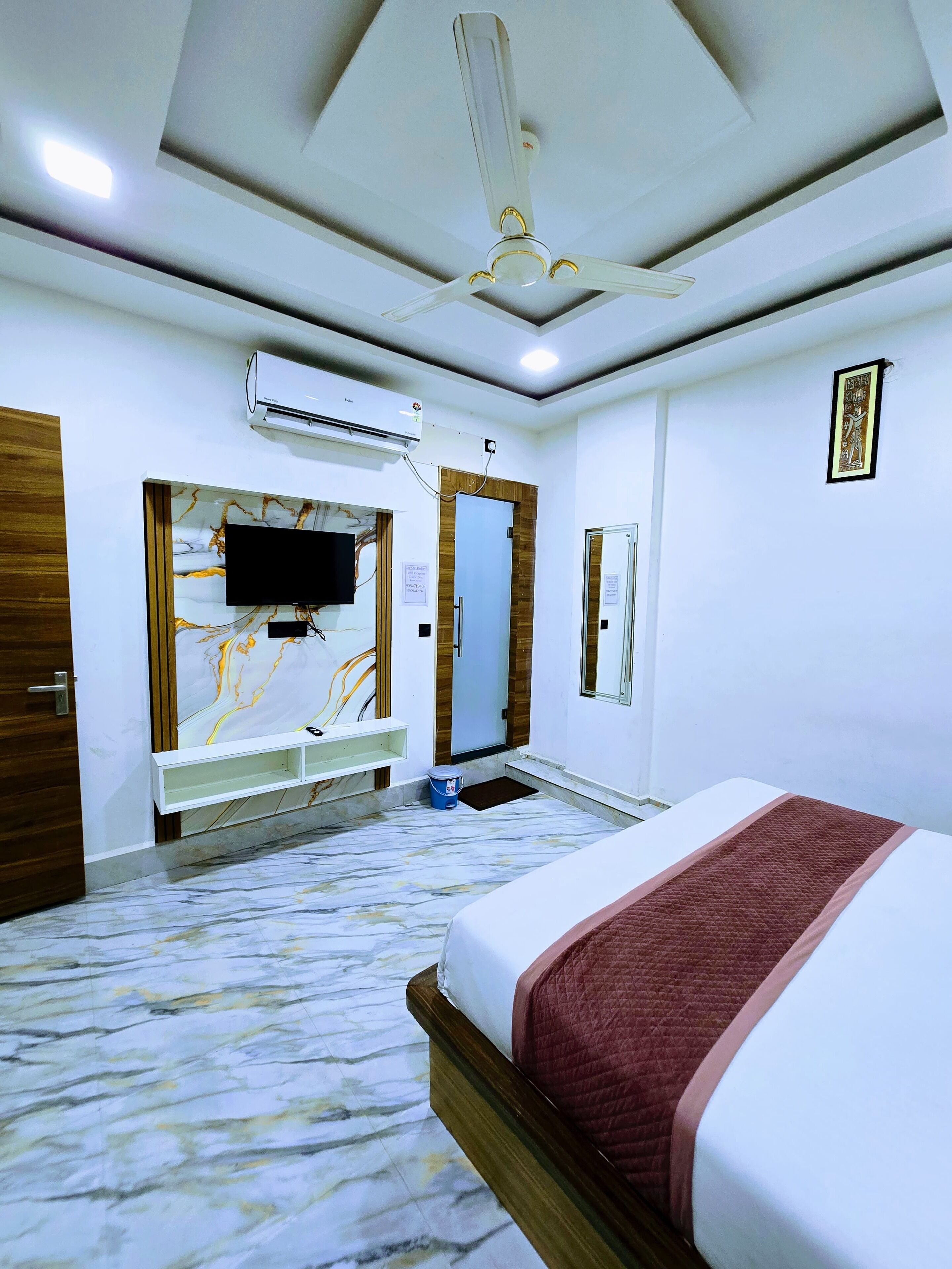 Une chambre d’hôtel équipée d’un lit, d’un ventilateur de plafond, d’un climatiseur, d’une télévision et d’un sol à motifs de marbre.