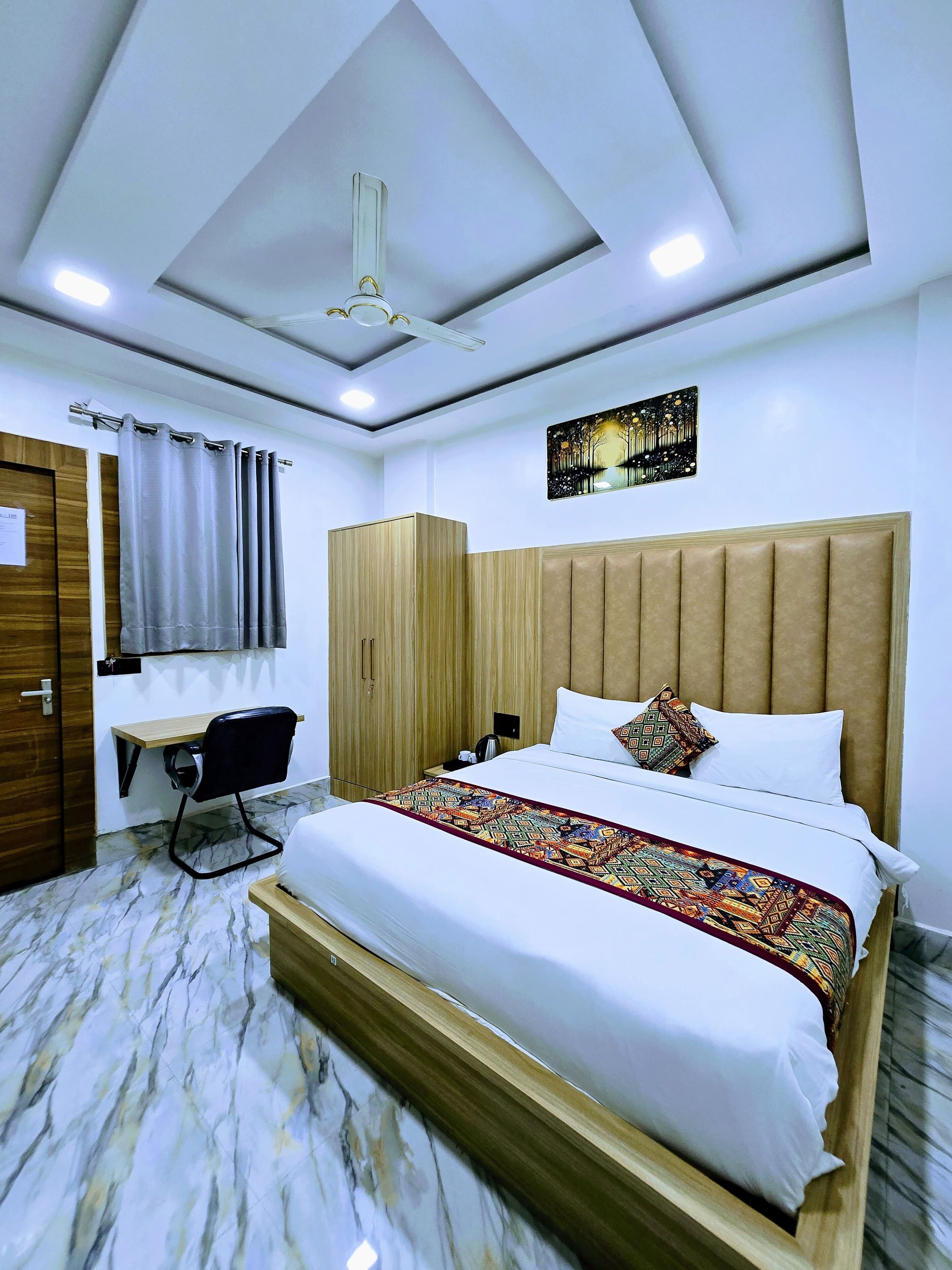 Quarto de hotel com cama, escrivaninha, cadeira, guarda-roupa e ventoinha no teto.