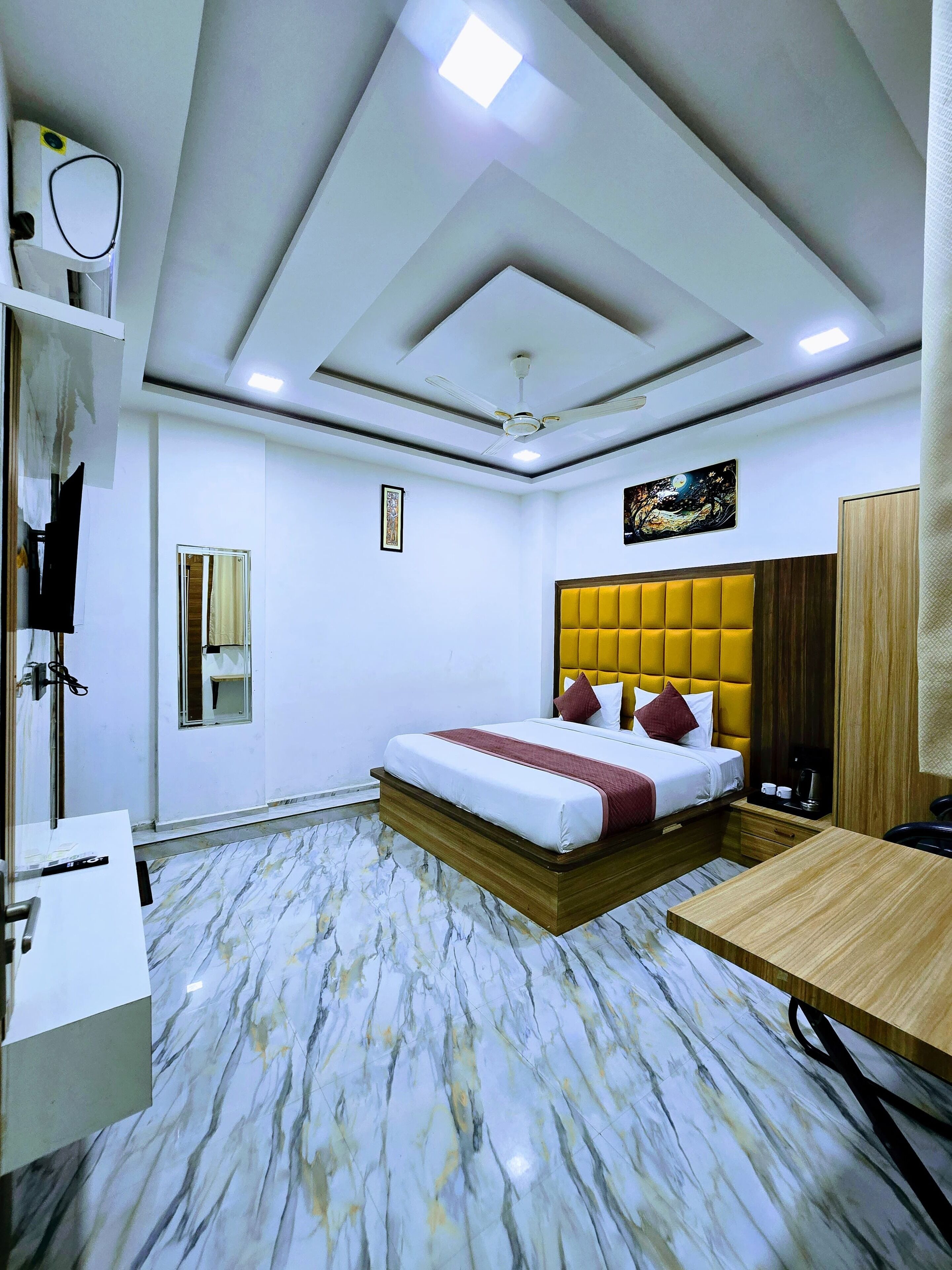Habitación de hotel con cama, escritorio, silla, ventilador de techo y mesita de noche.