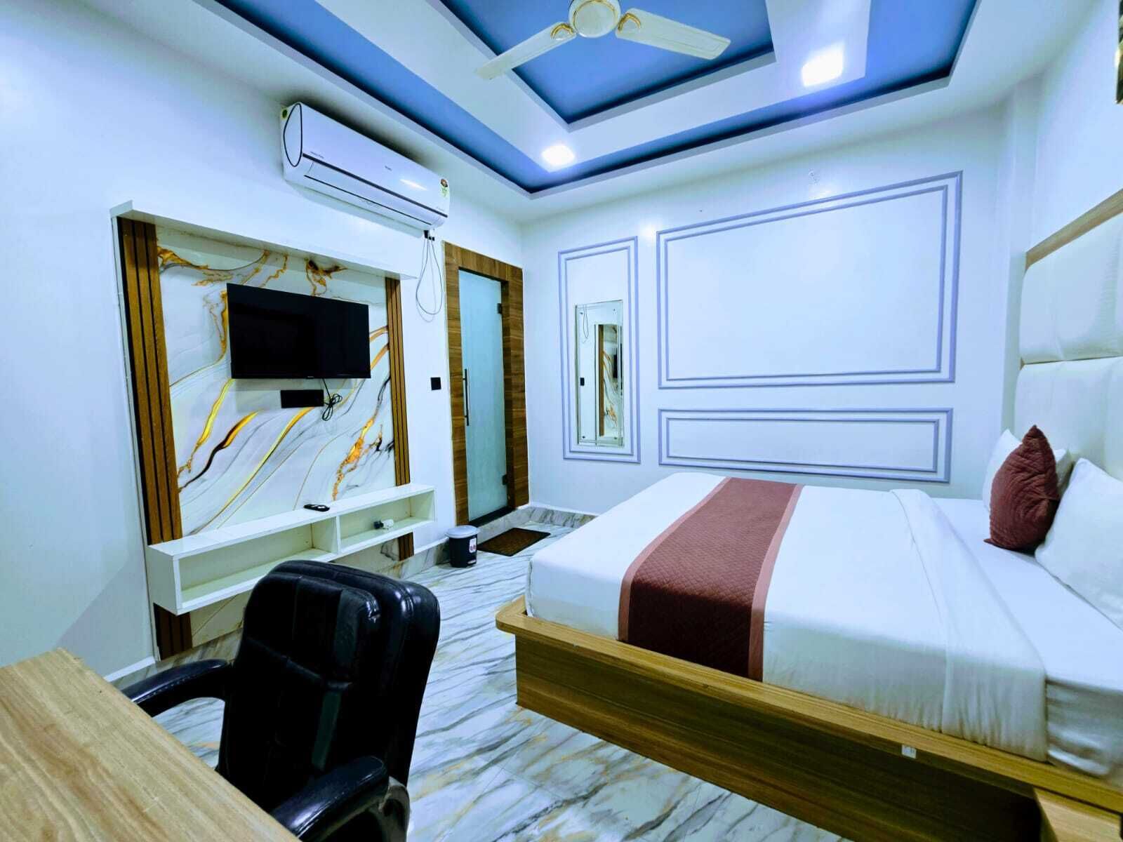 A hotel room with a bed, a desk, a chair, a TV, and an air conditioning unit.