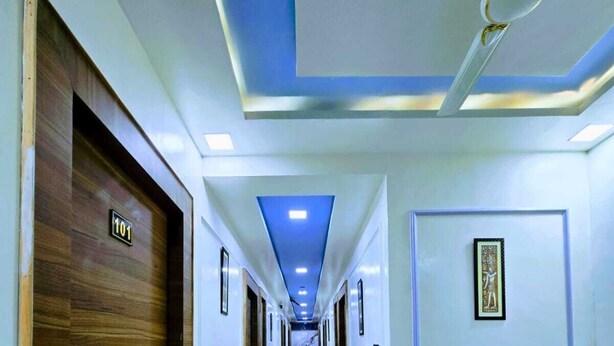 A hotel hallway with a marble floor, wooden doors, and a blue ceiling with recessed lighting. - Hotel Aaarav Grand - Mathura Vrindavan (Mathura)