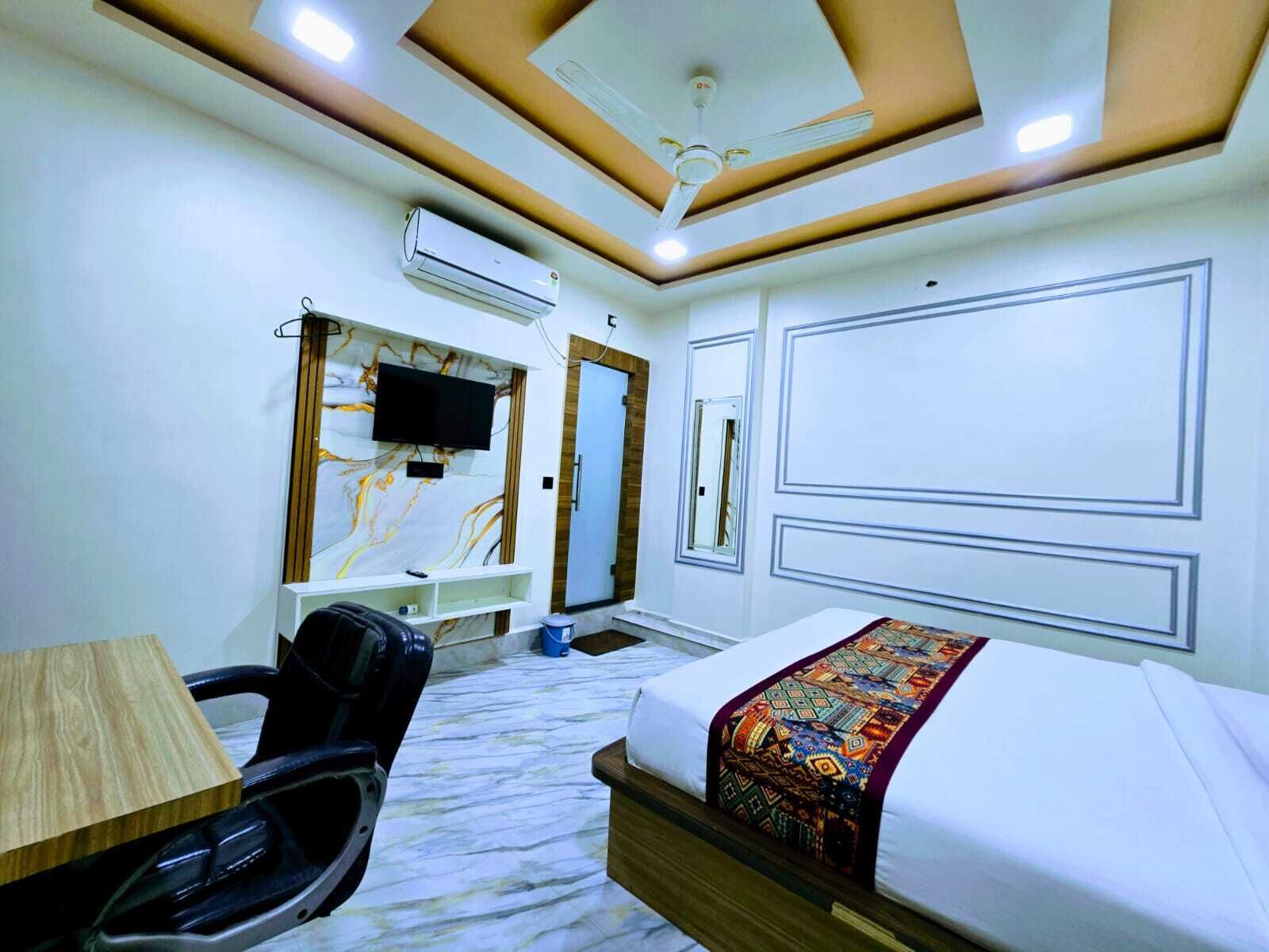 A hotel room with a bed, a desk, a chair, a TV, and an air conditioning unit.