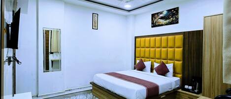 A hotel room with a bed, a desk, a chair, a ceiling fan, and a painting on the wall.