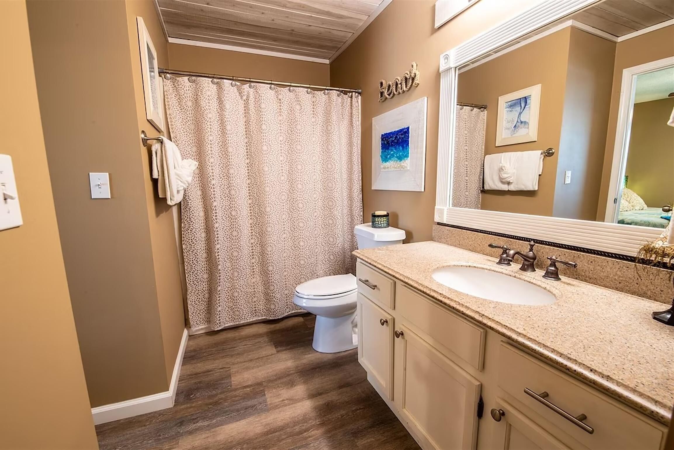 A bathroom with a shower curtain, toilet, sink, and vanity.