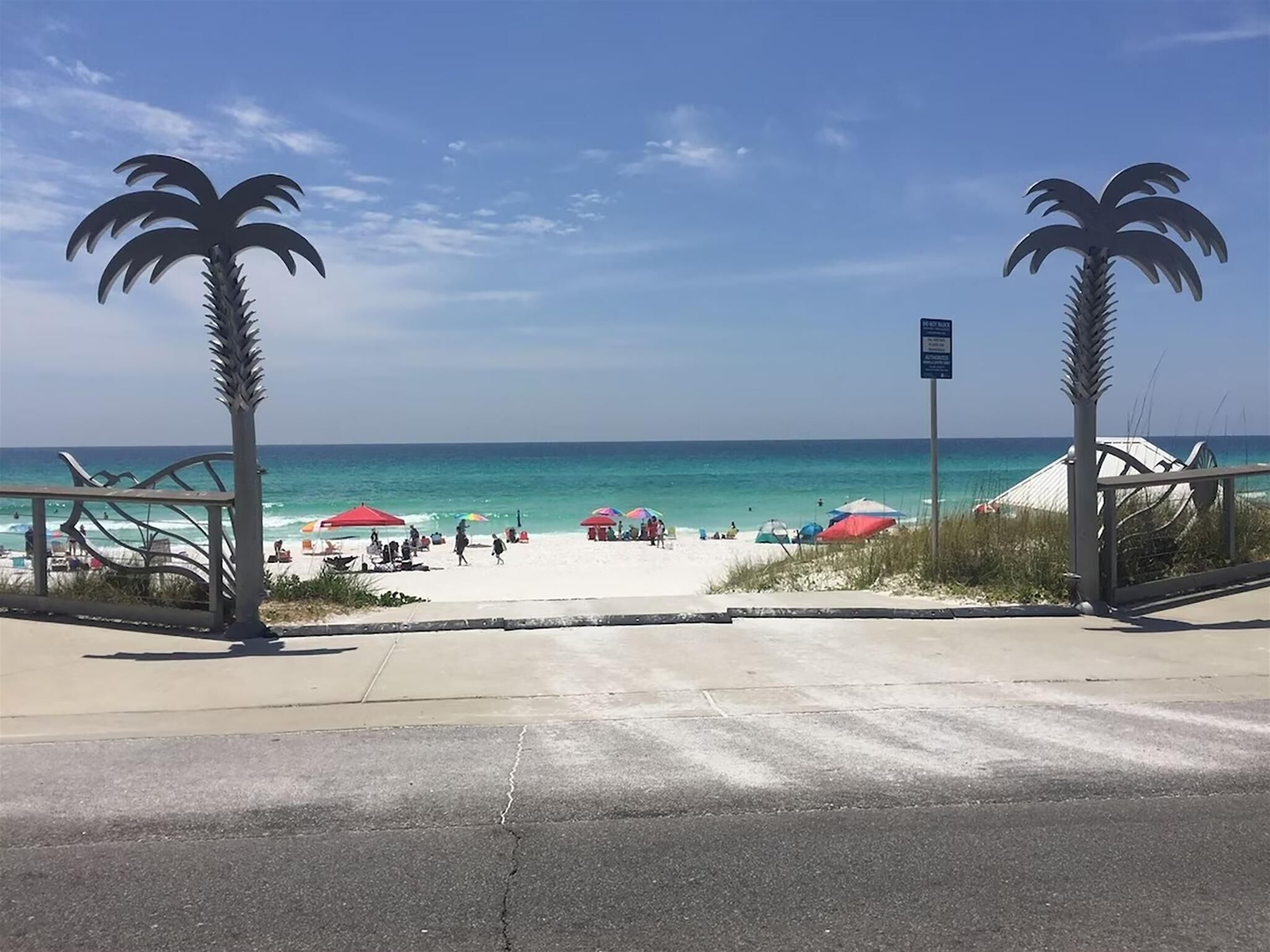 Una entrada a la playa con palmeras, cielo despejado y vista al océano.