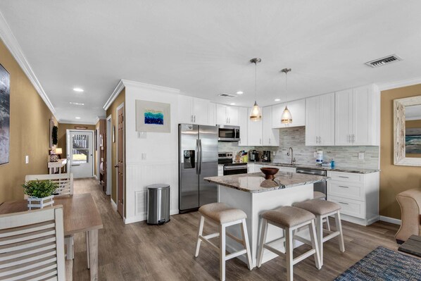 A modern kitchen with white cabinets, stainless steel appliances, and a central island with stools. - Seacove 6A (Miramar Beach)