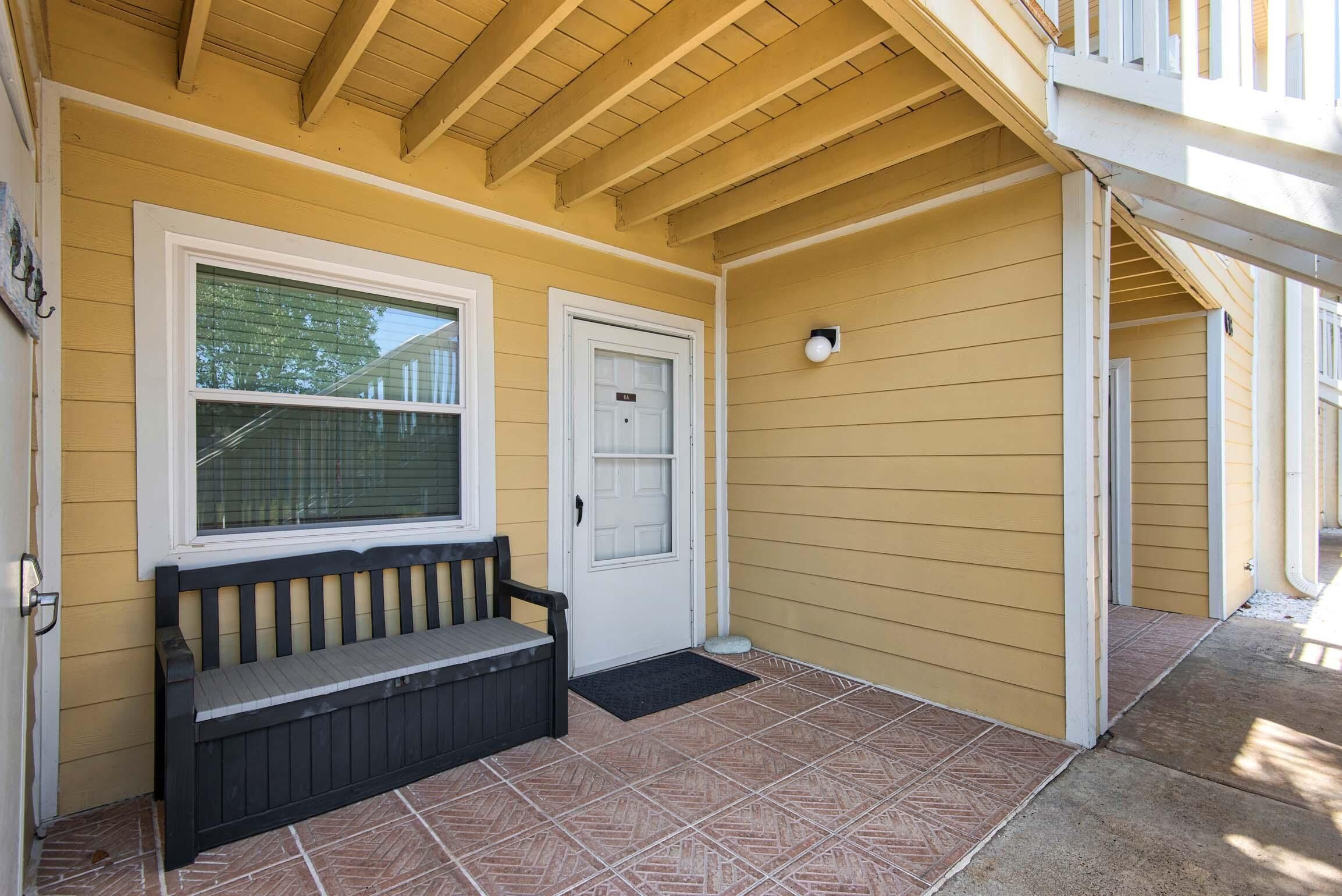 A yellow building with a covered porch, a bench, and a door with a mailbox.