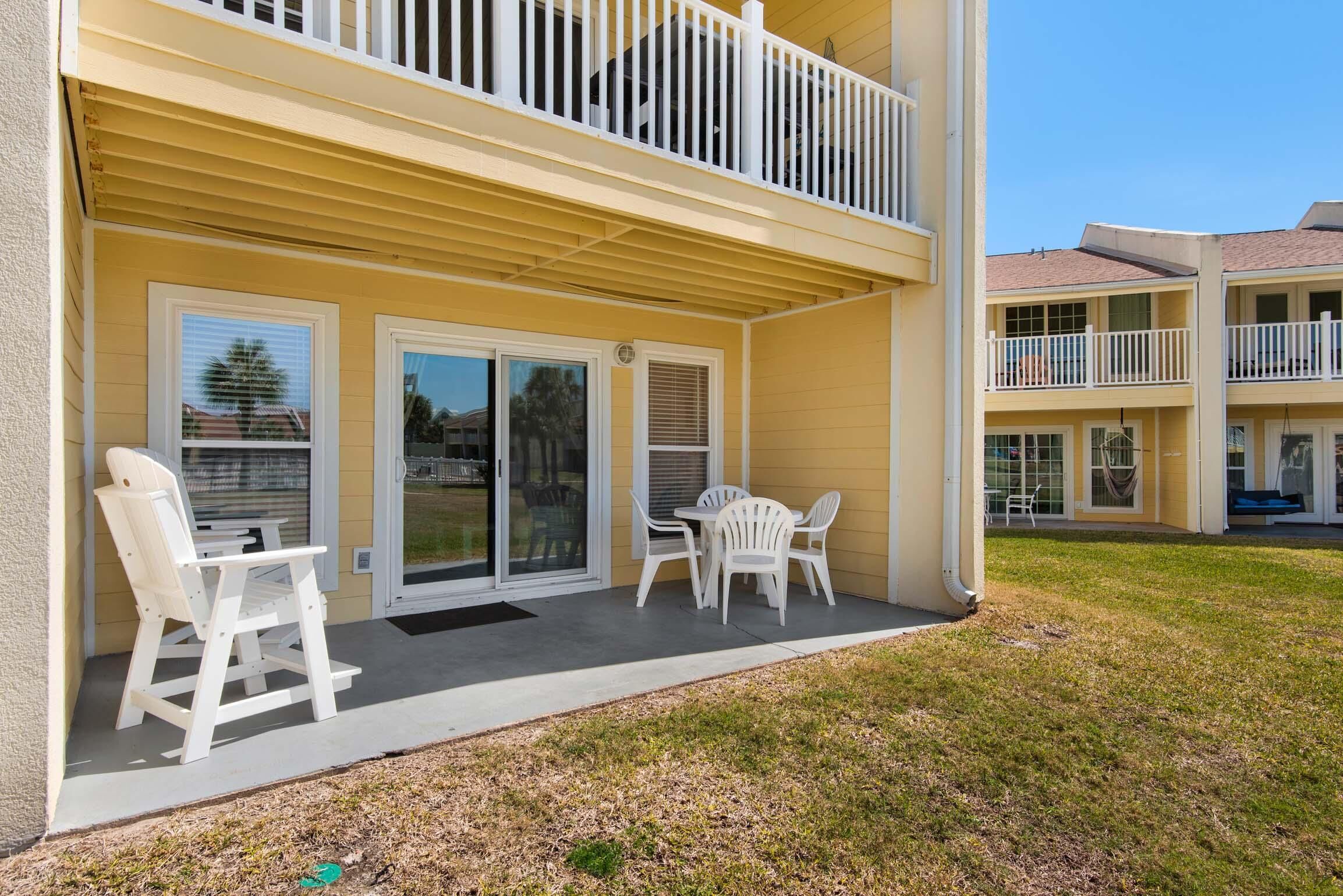 A yellow building with a balcony, sliding glass doors, and outdoor seating with white chairs.