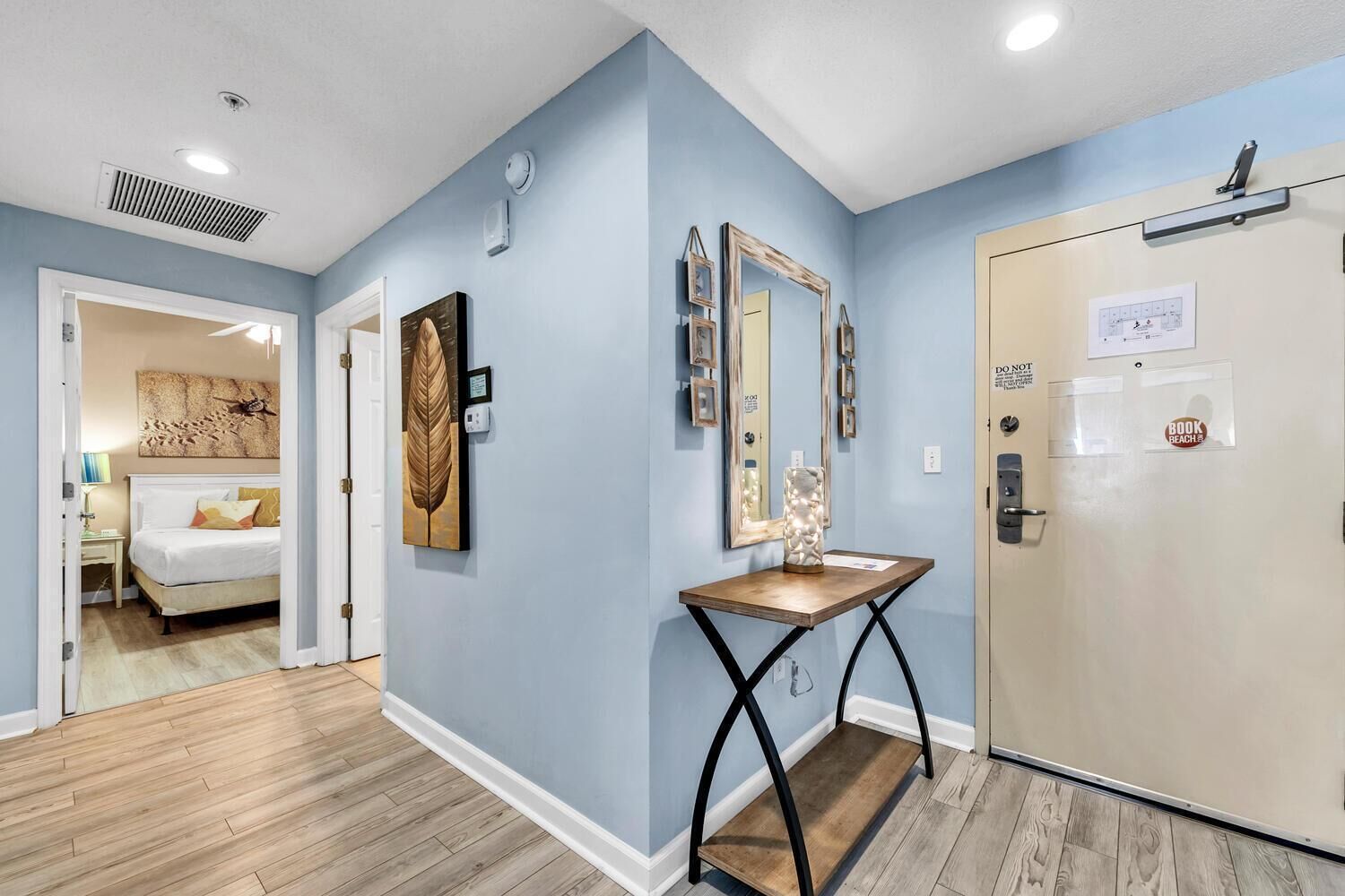 A hotel hallway with a bed, a wooden console table, and a door with a sign.