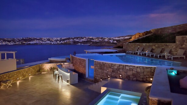 Ein Infinity-Pool mit Blick auf die Küstenlinie, Steinwände und Liegestühle.