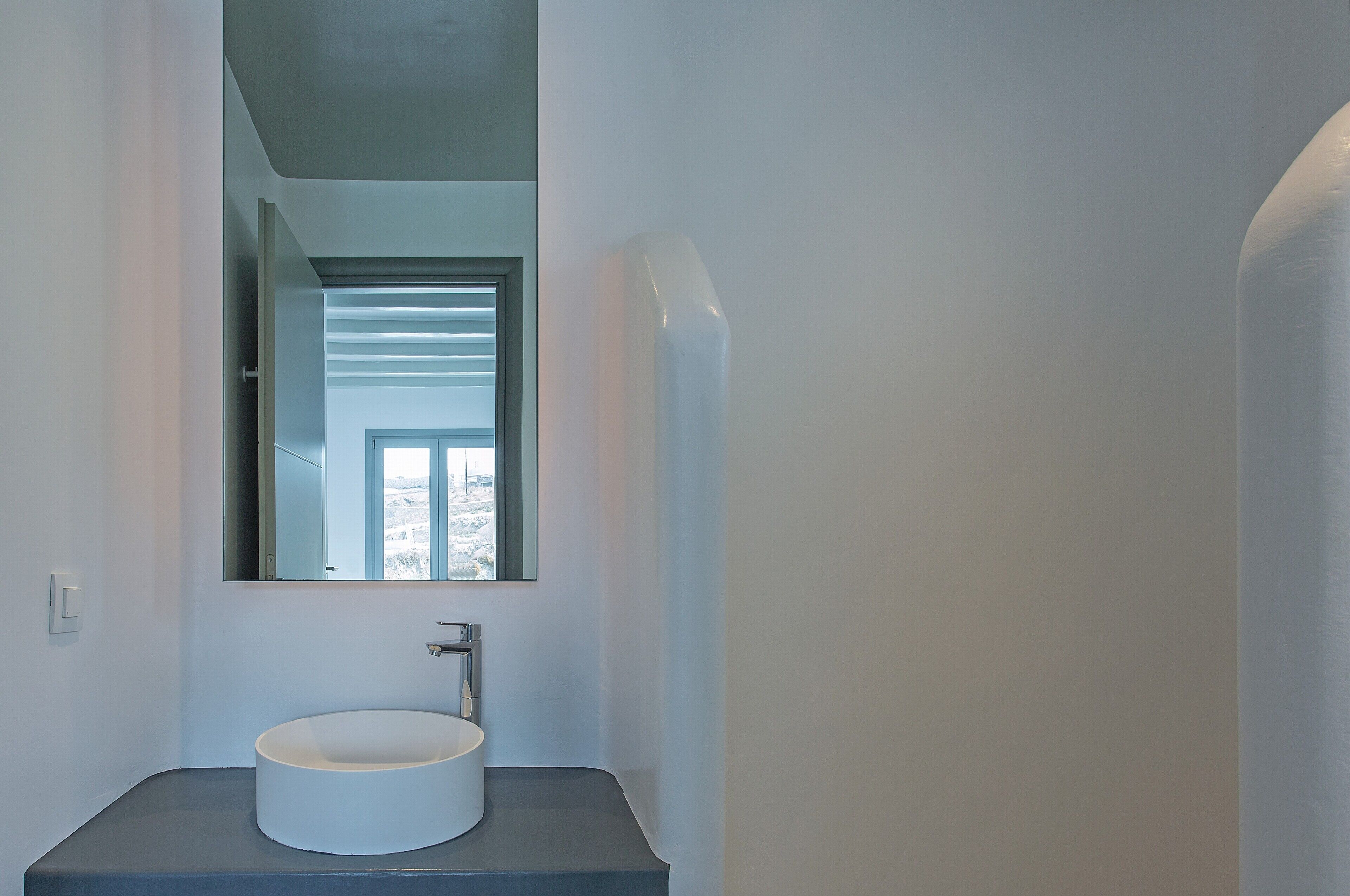 A modern bathroom with a round sink, a mirror, and a window.