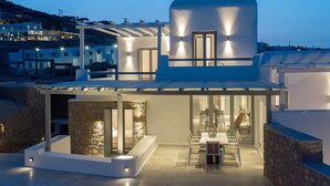 Ein modernes Haus mit Terrasse, Steinmauern und einem Essbereich mit Stühlen und Tisch.