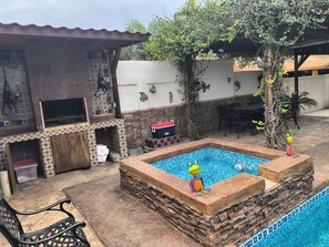 pool area with a rectangular pool, stone ledge, and adjacent seating area with a table and chairs.